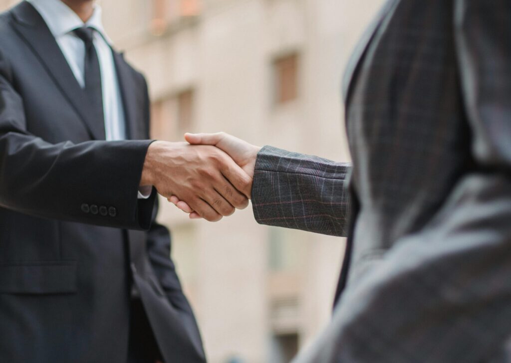 Business professionals greeting each other with a handshake outdoors, symbolizing partnership.